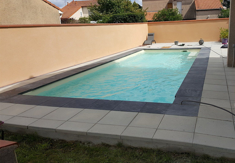 Piscine traditionnelle à Tarbes avec terrasse dallée et margelles foncées par SARL DSR Construction